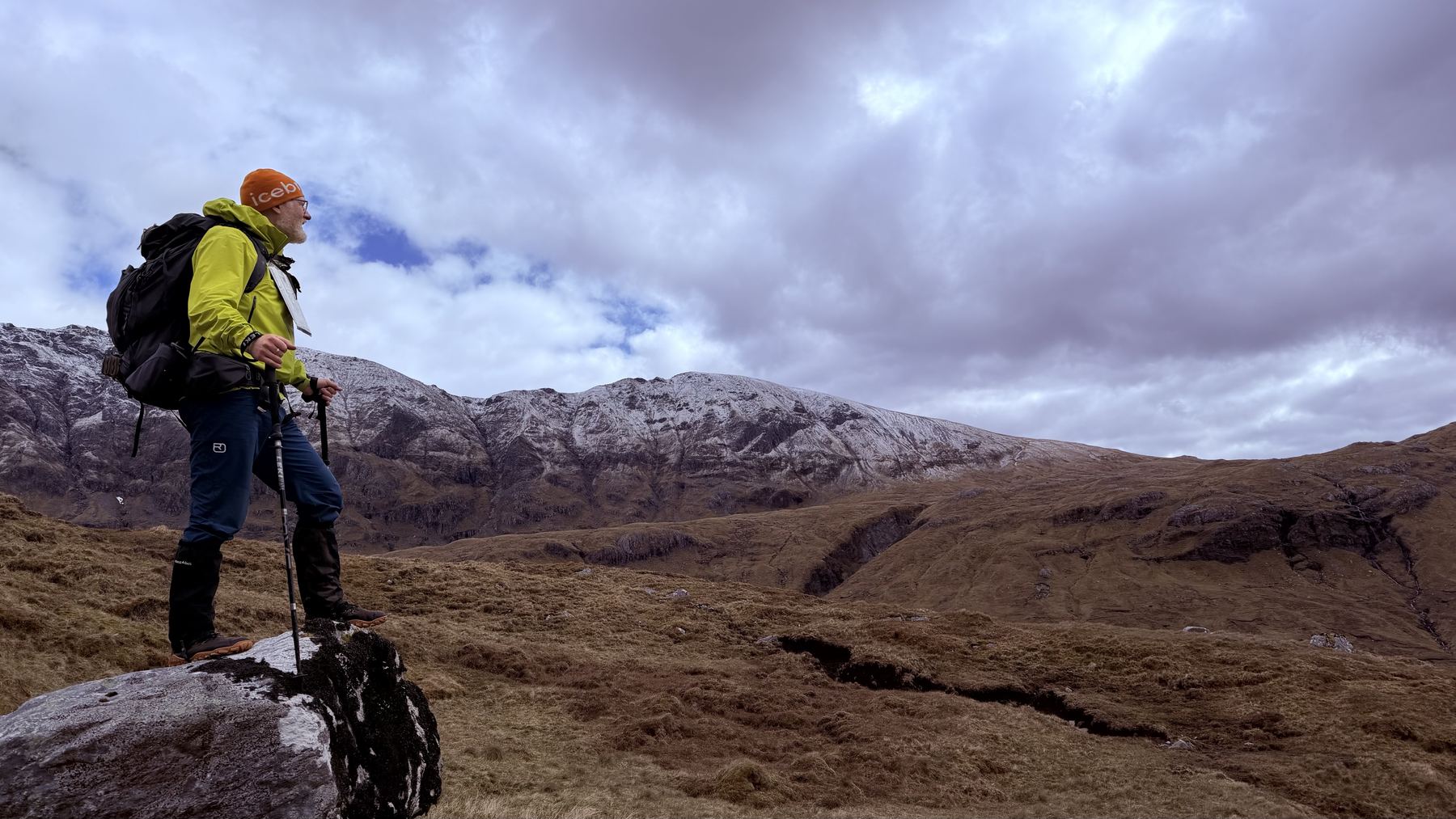 Me on a rock below a snow-dusted ridge, looking out across the glen